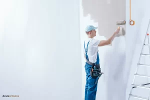 Un artisan peintre peint un mur au rouleau.